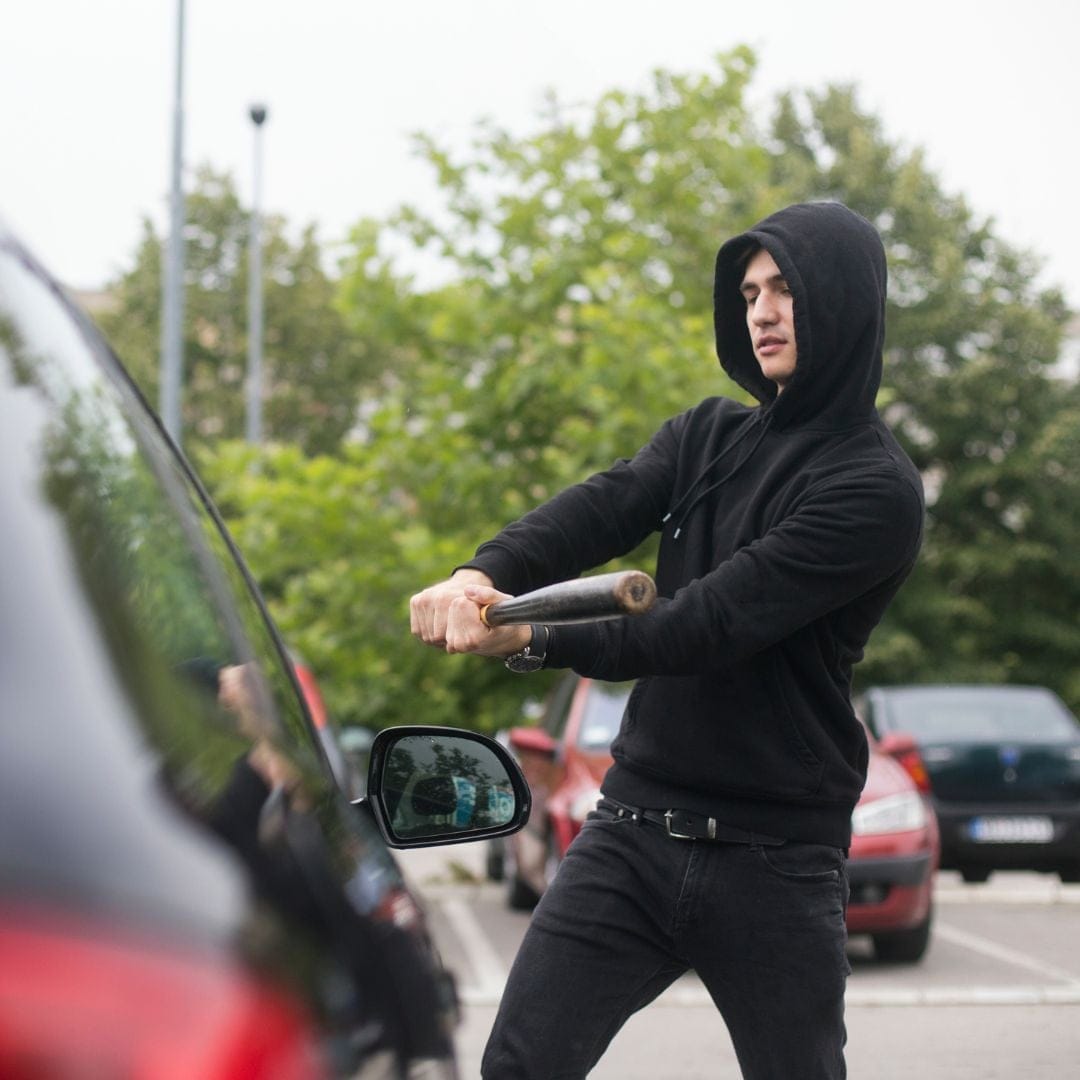A young man hitting a car with a bat