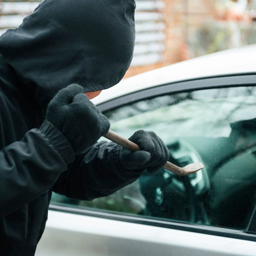 A person about to hit a car window with a crowbar